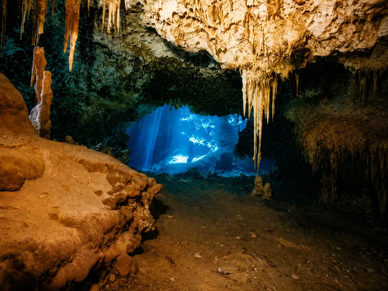 Scuba divers exploring an ancient crystal clear underwater cavern with dive lights